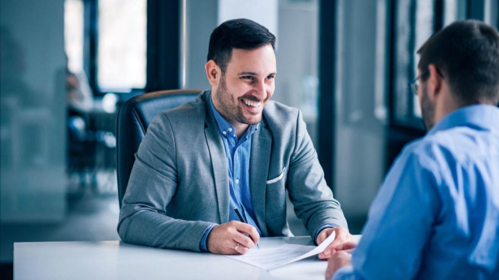 A banker sits at a desk and smiles while working with a customer.